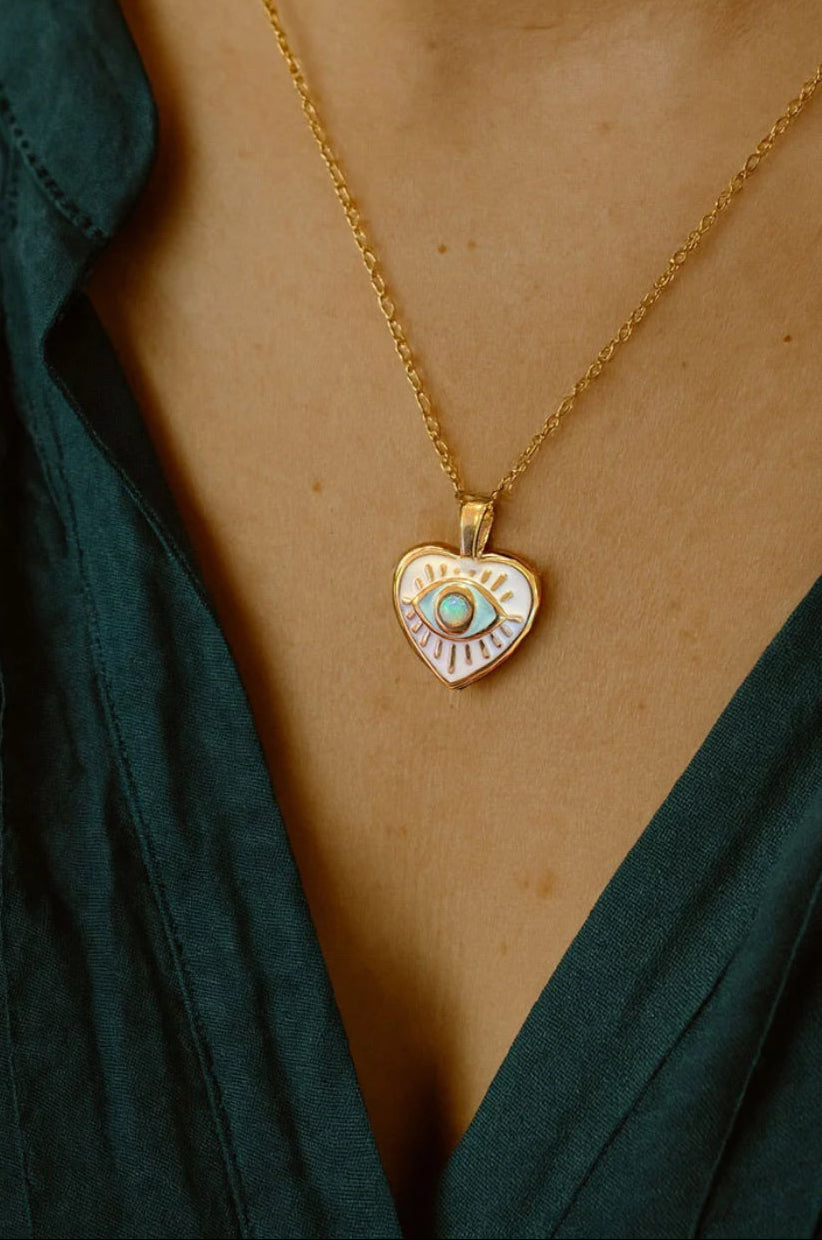 Gold necklace with a heart-shaped pendant worn by a person in a green top.